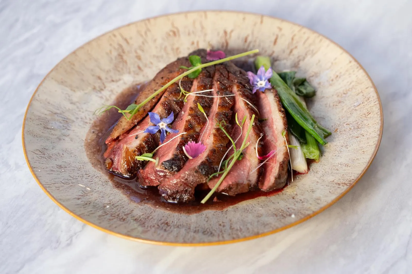 Entrecôte grillée tranchée, légumes verts et fleurs comestibles